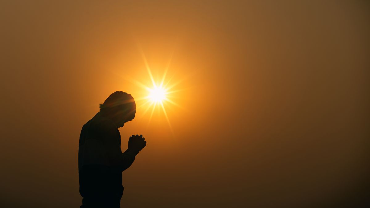 A person praying with the sun on the background